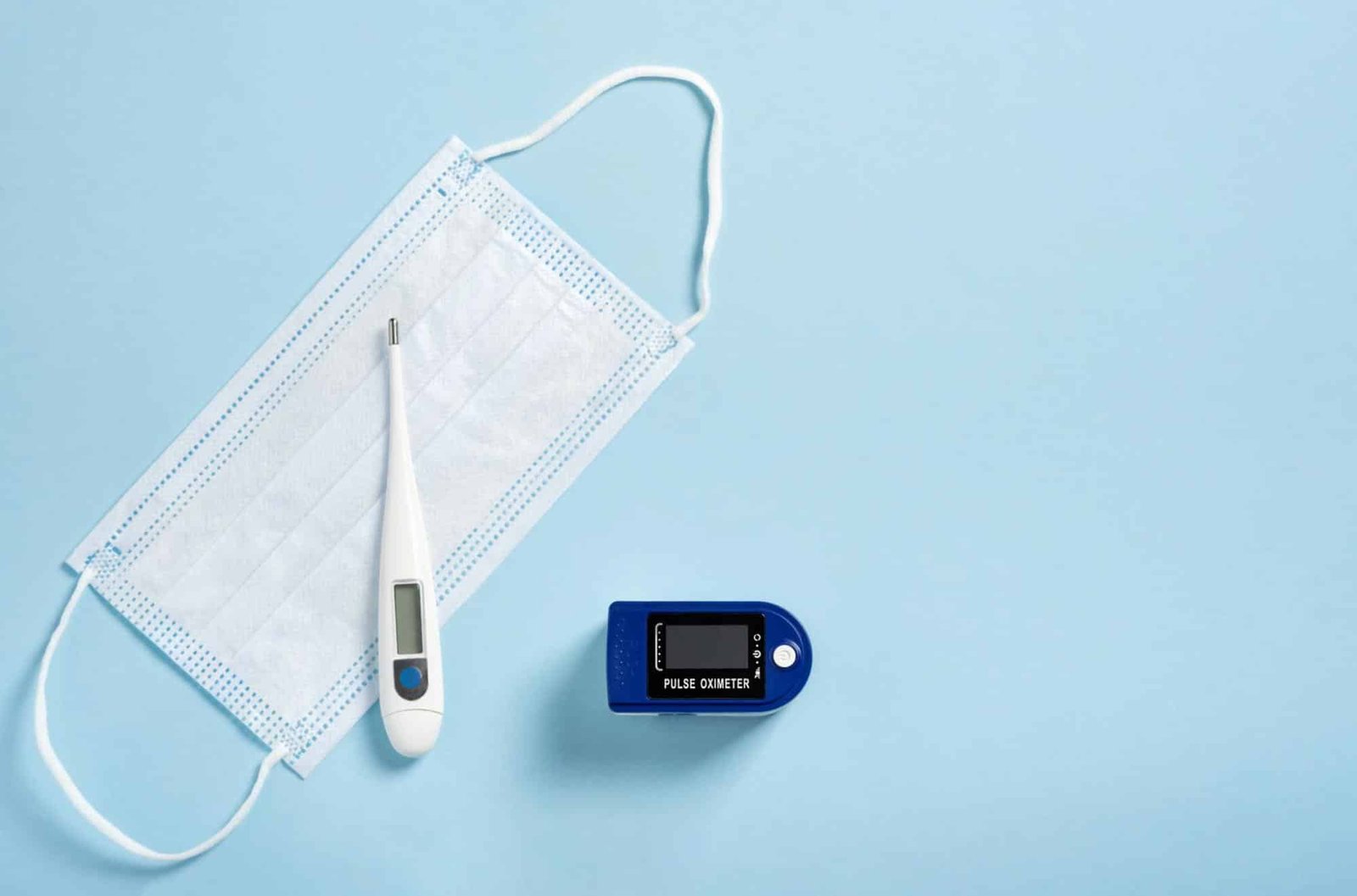 pulse oximeter, face mask, and thermometer on blue surface