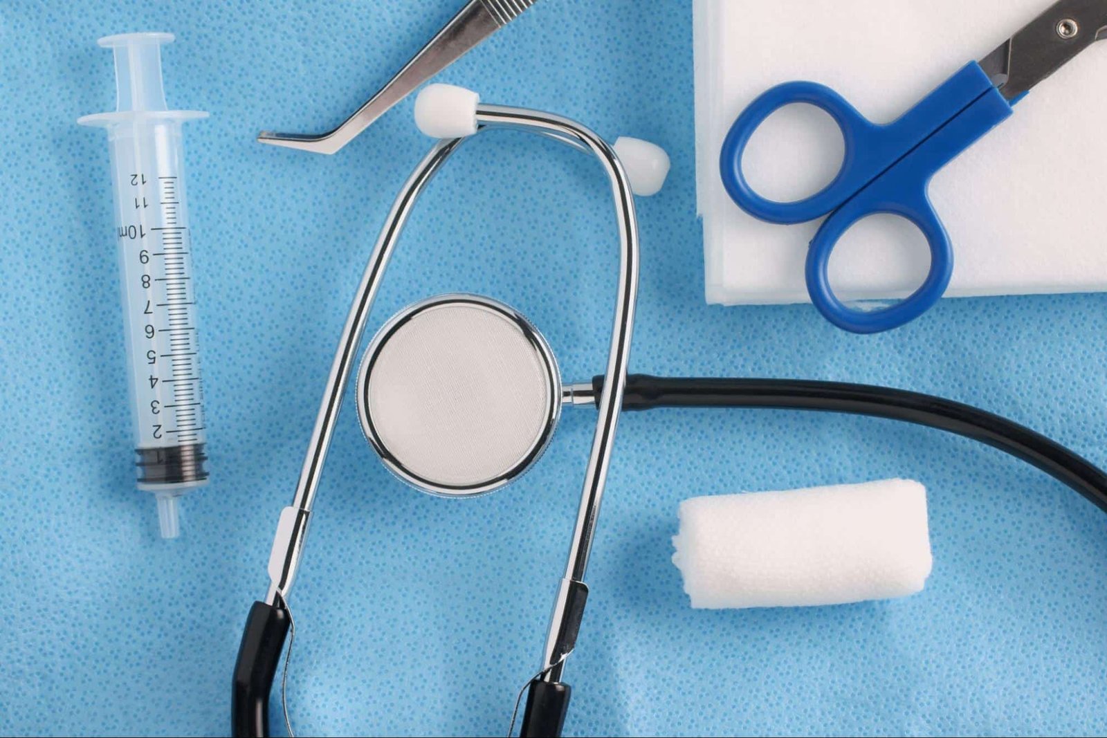 stethoscope, syringe, scissors, and gauze on a blue surface