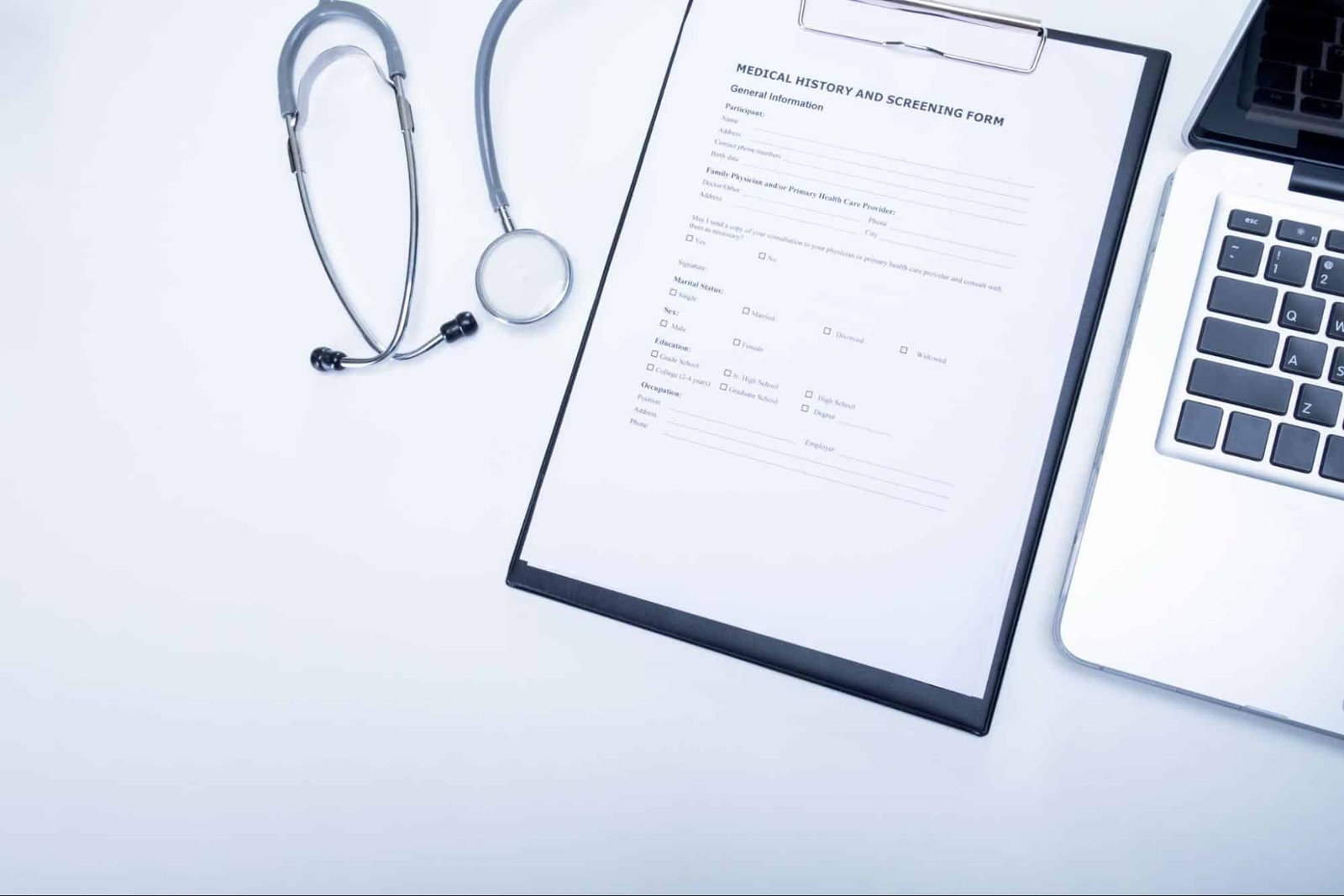 medical history and screening form, stethoscope, and laptop on a primary care provider’s desk