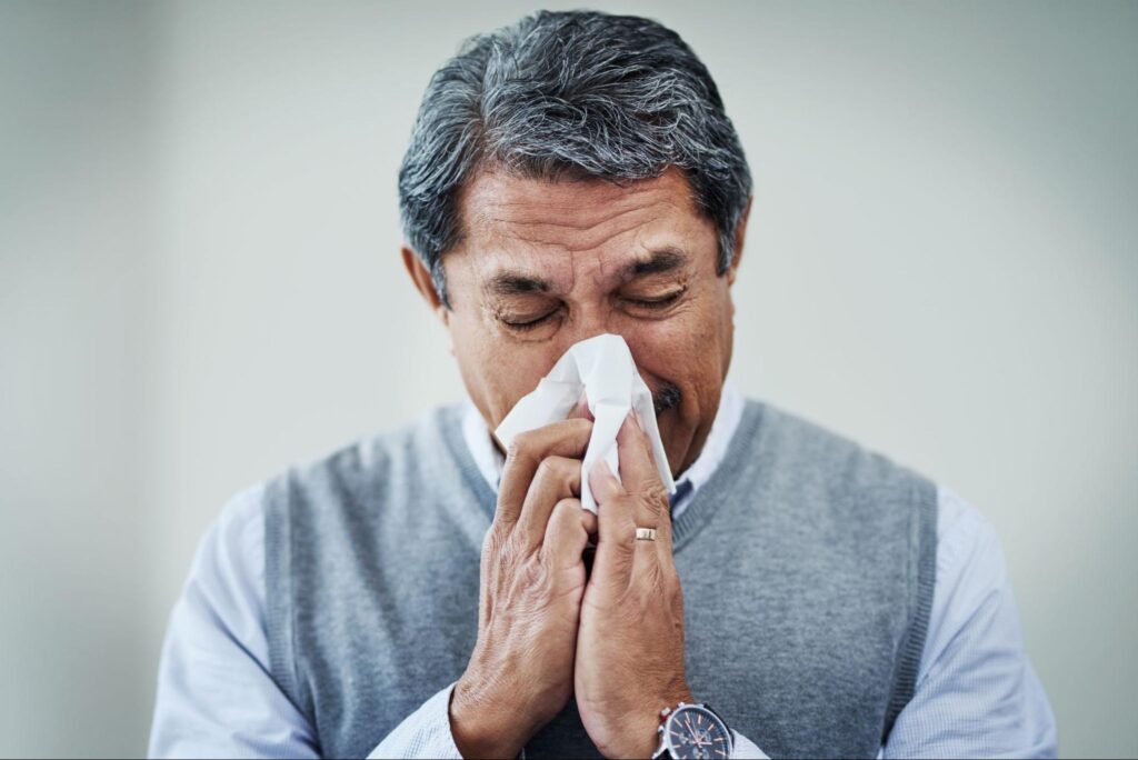 Man blowing his nose into a tissue with flu symptoms, representing a patient seeking care at an evening clinic near me for after-hours illness treatment.