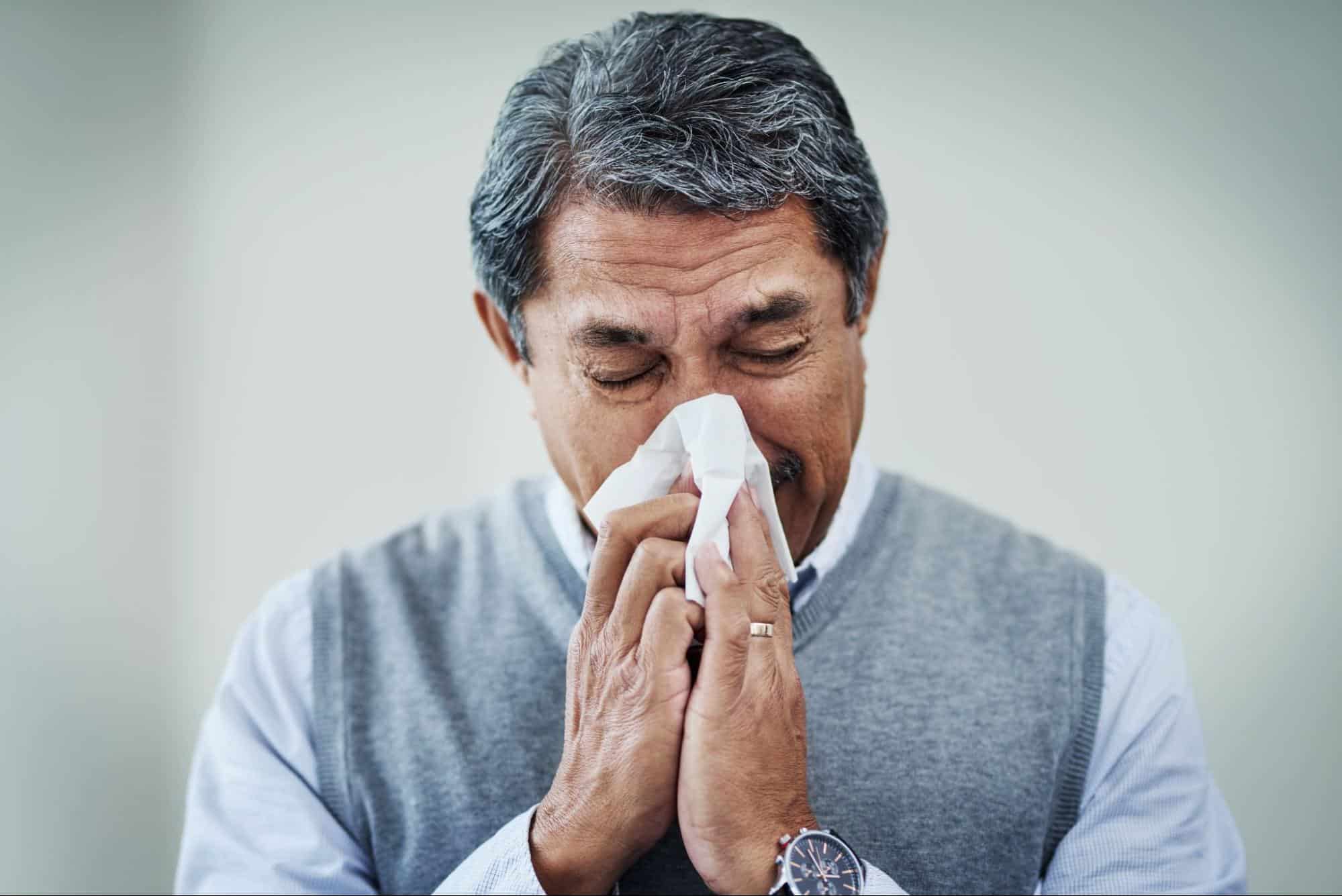 Man blowing his nose into a tissue with flu symptoms, representing a patient seeking care at an evening clinic near me for after-hours illness treatment.