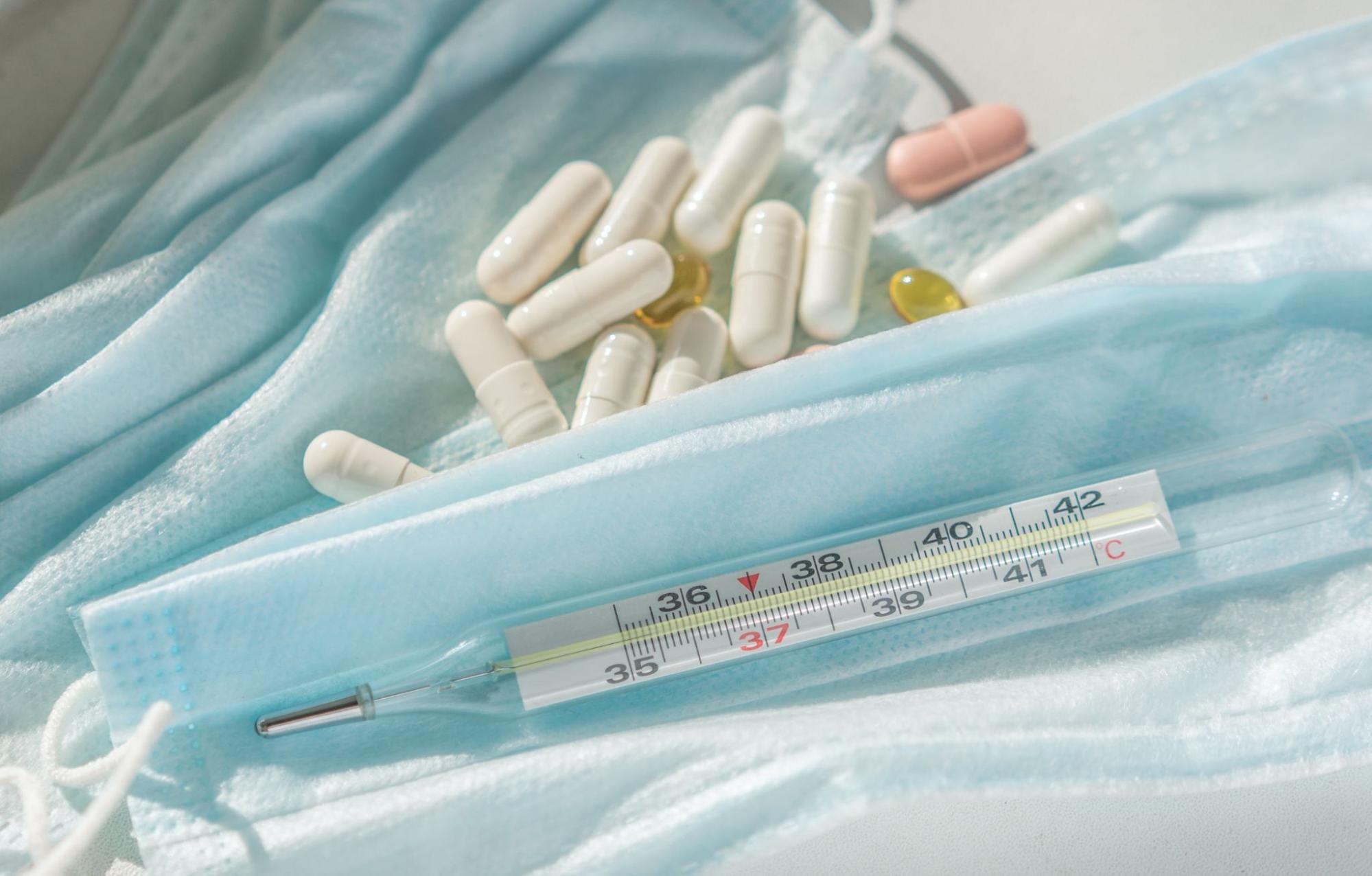 Thermometer and assorted pills on medical mask