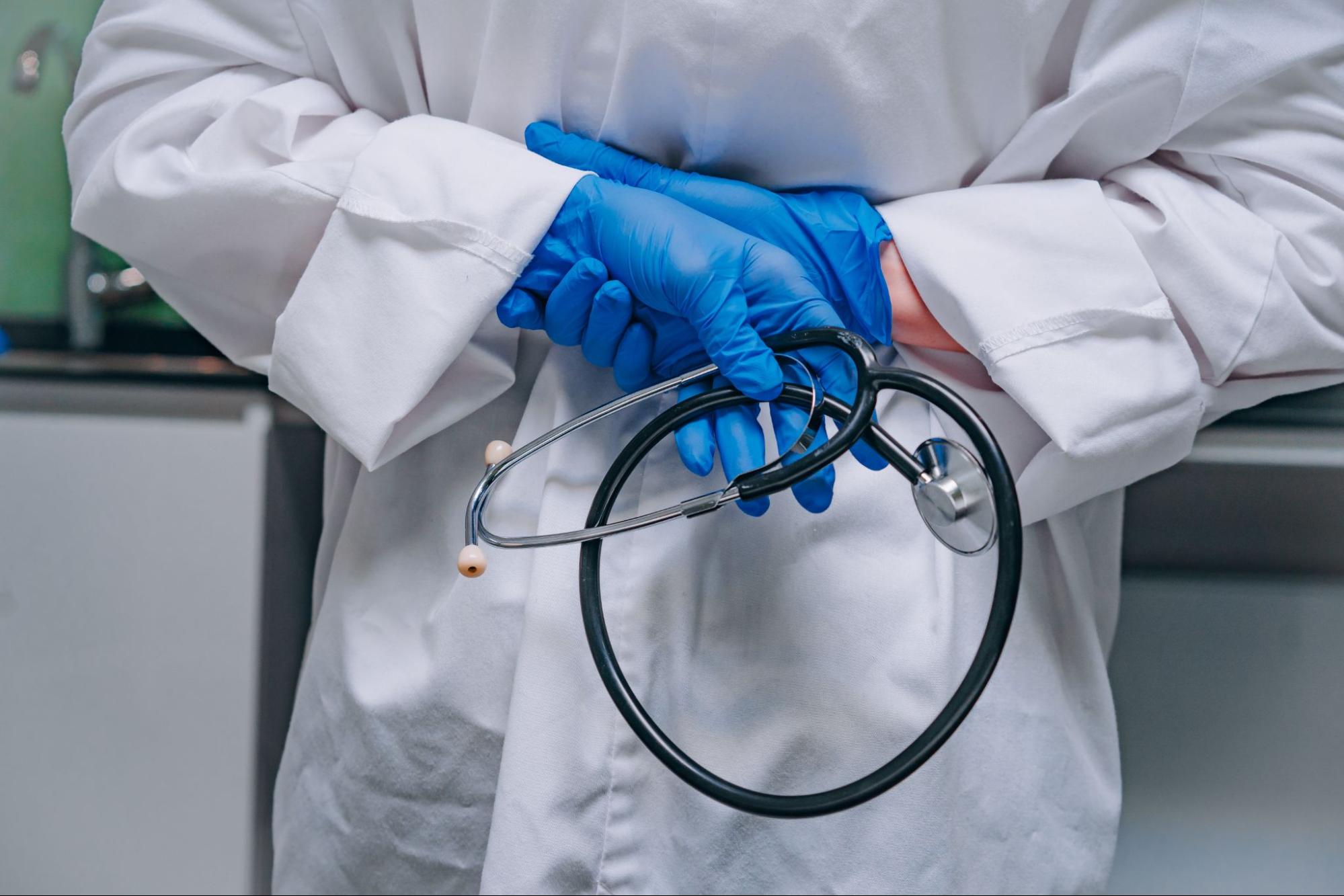 Primary care provider in white coat wearing blue gloves holding a stethoscope