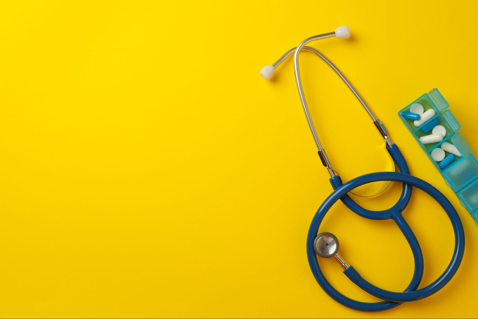 Stethoscope with pills on yellow background