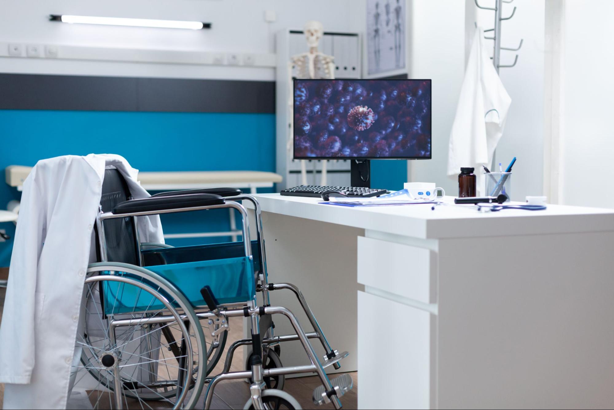 Clean exam room with wheelchair, desk, and monitor reflecting an after hours healthcare clinic environment