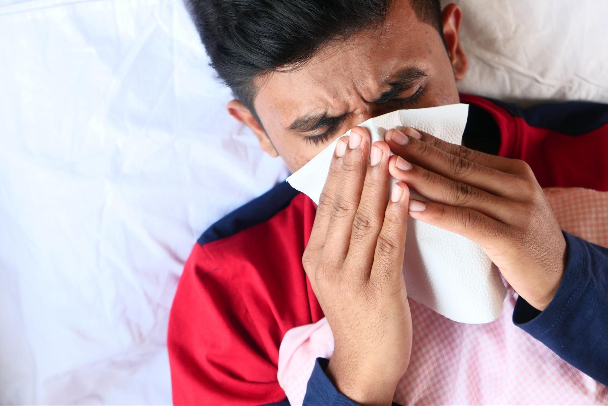 Sick man blowing nose in bed, common illness treated at an after hours medical clinic