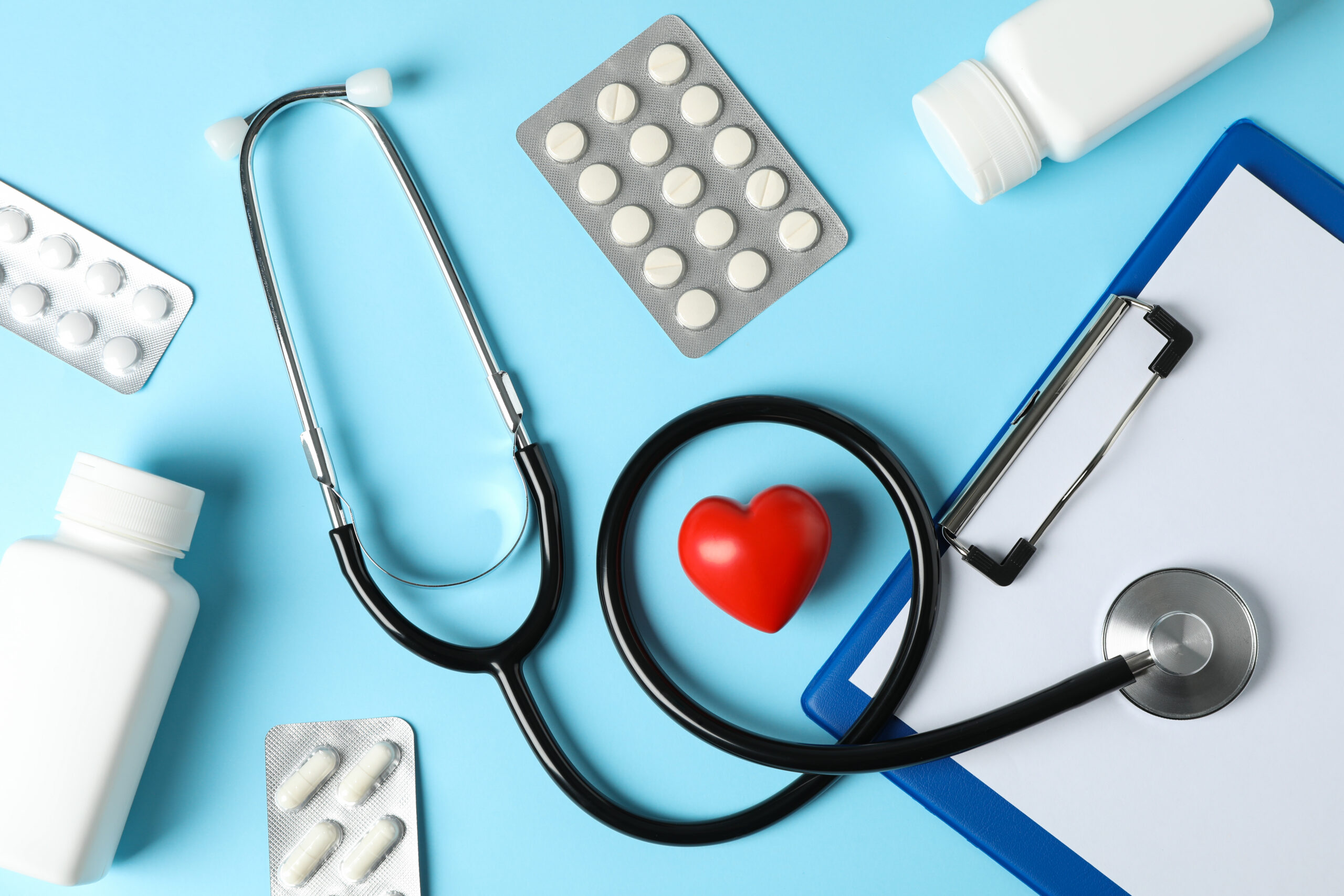 Stethoscope, tablet, heart and medicine on blue background
