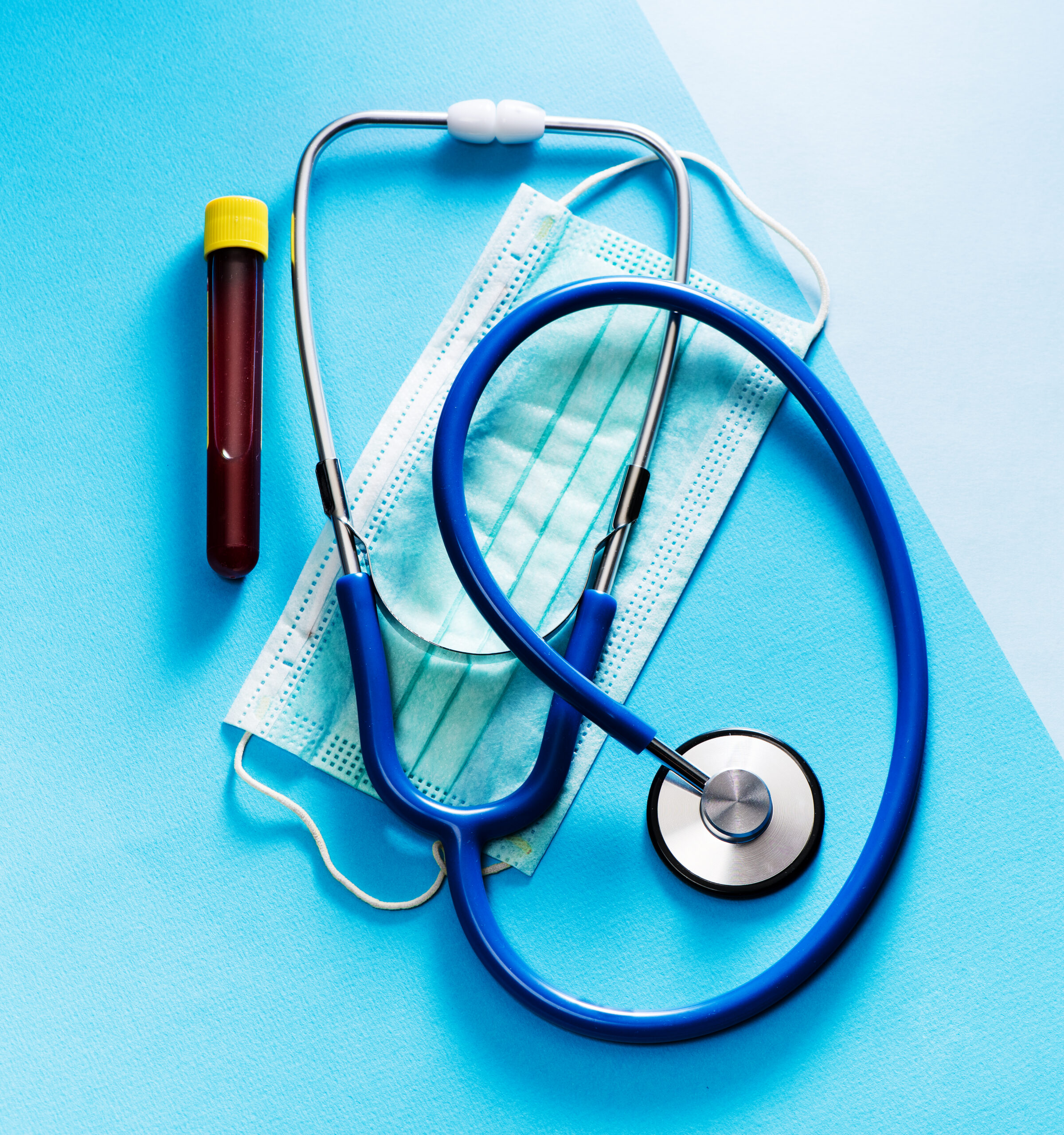 Test tube with blood sample, stethoscope and mask on blue background